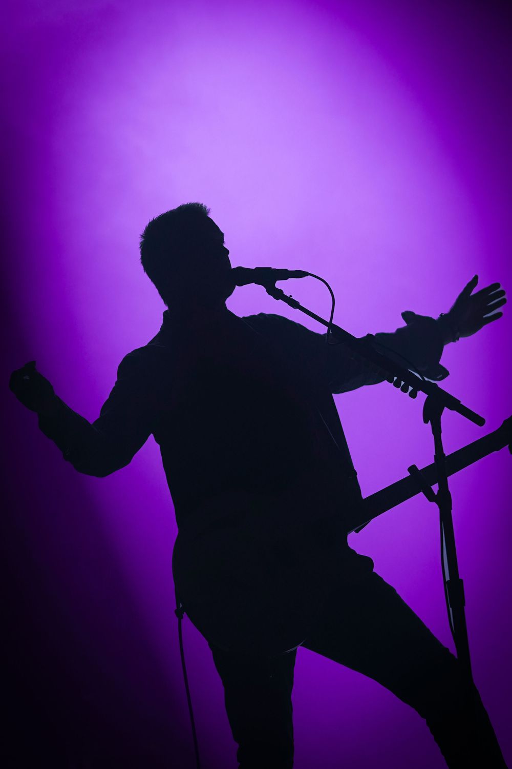 Silhouette of a male singer performing on stage with a microphone against a vibrant purple backlit background.