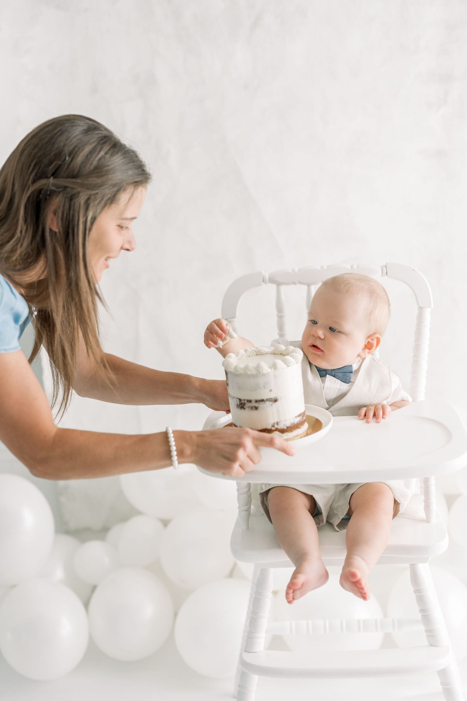 Maman présentant le gâteau à bébé assis dans sa chaise haute antique blanche