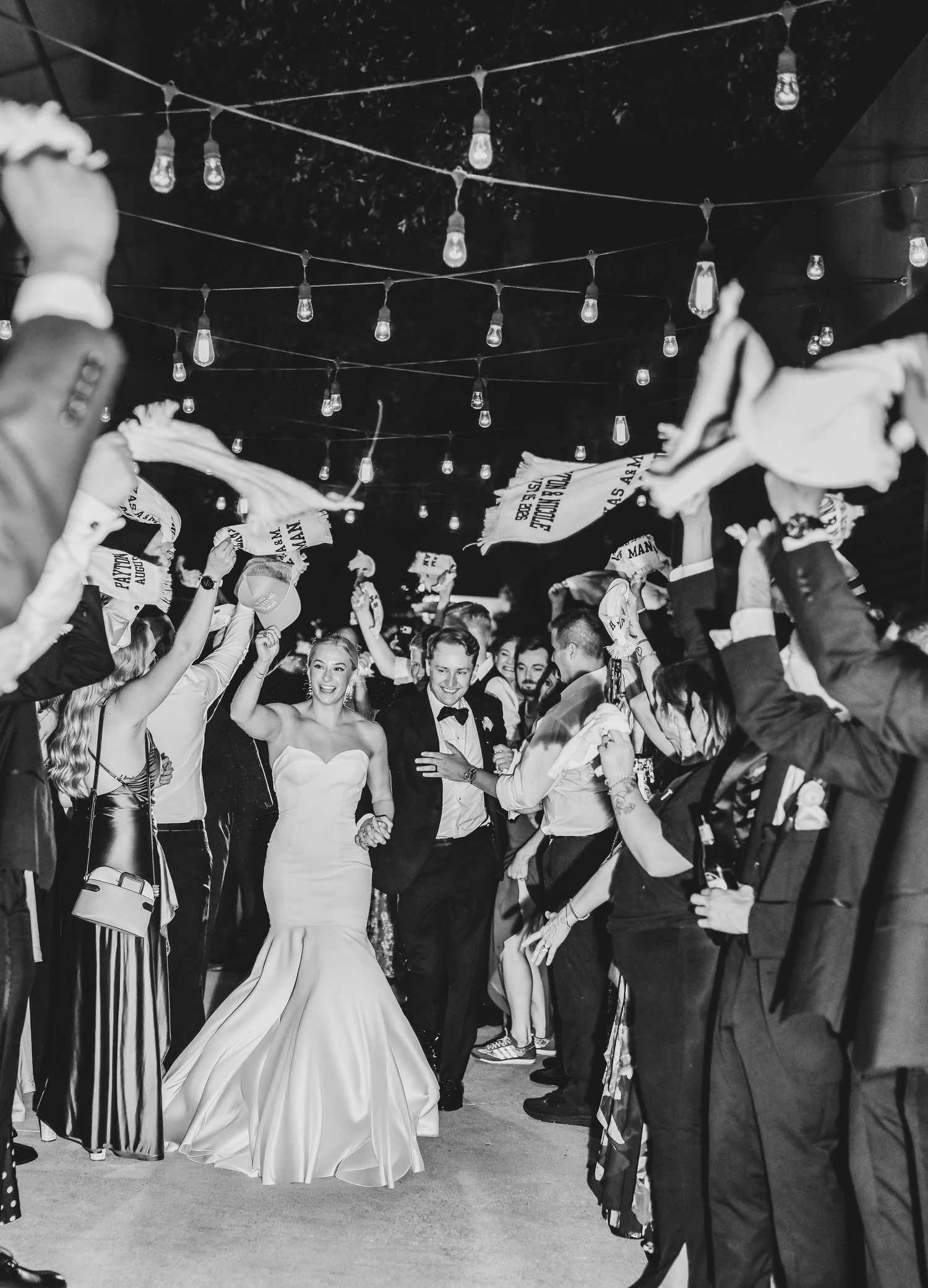 excited bride and groom exit their wedding reception through their friends and family waiving aggie towels
