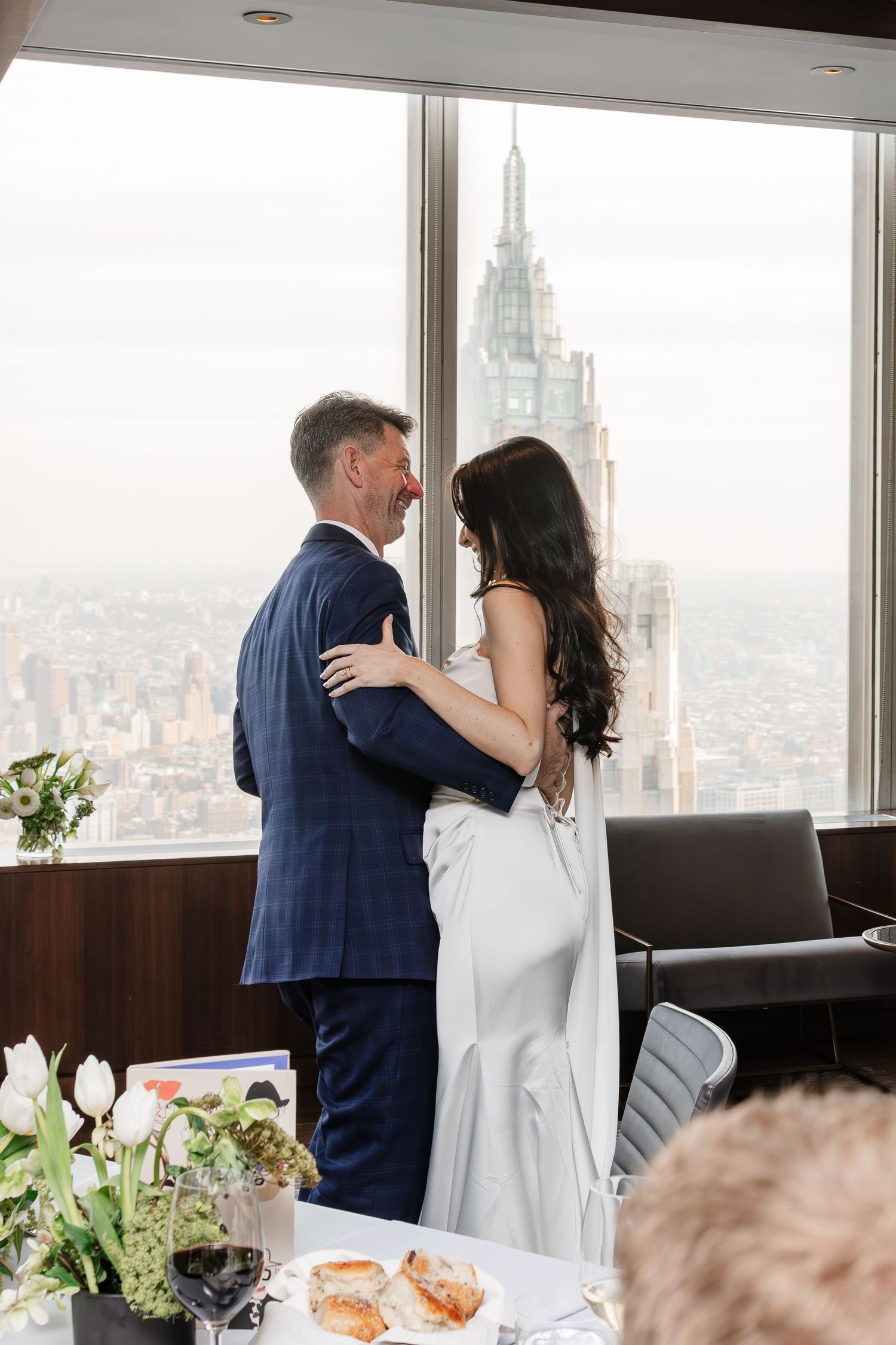 Couple sharing a romantic embrace in elegant wedding attire with a stunning New York City skyline view.