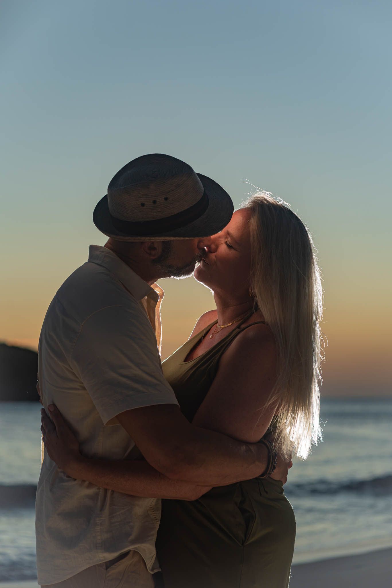 Couple holding hands on beach, woman wearing elegant purple gemstone engagement ring, romantic ocean background.