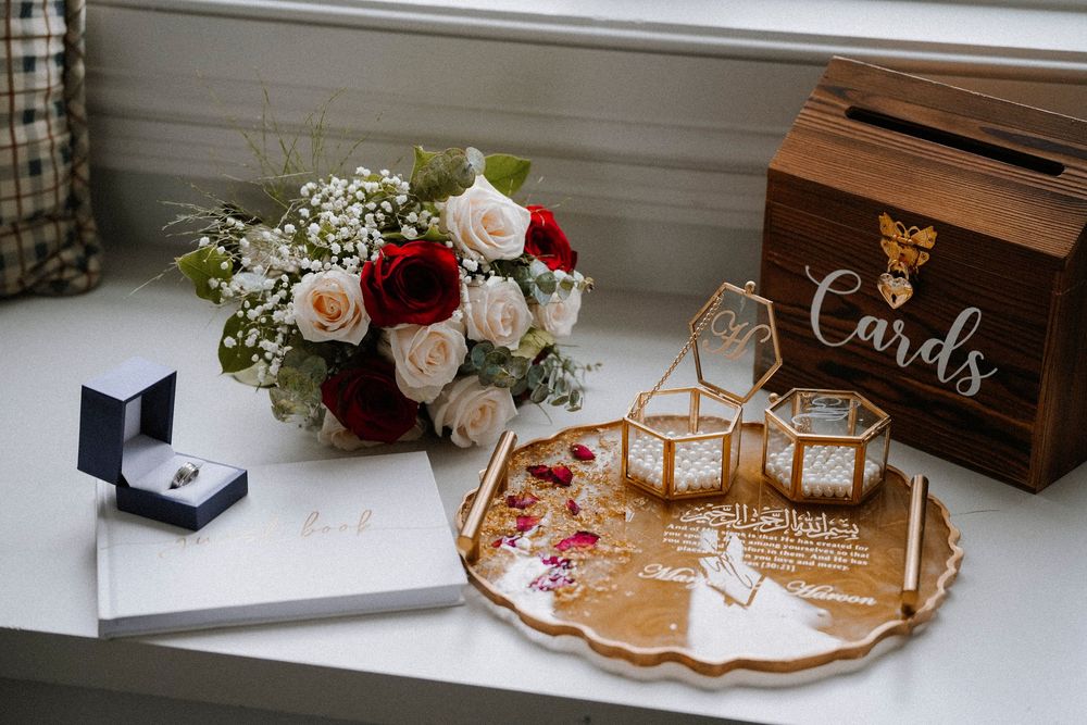 Elegant wedding flat lay with red and white roses, gold geometric terrariums, a Cards box, and ring jewelry on a white surface.