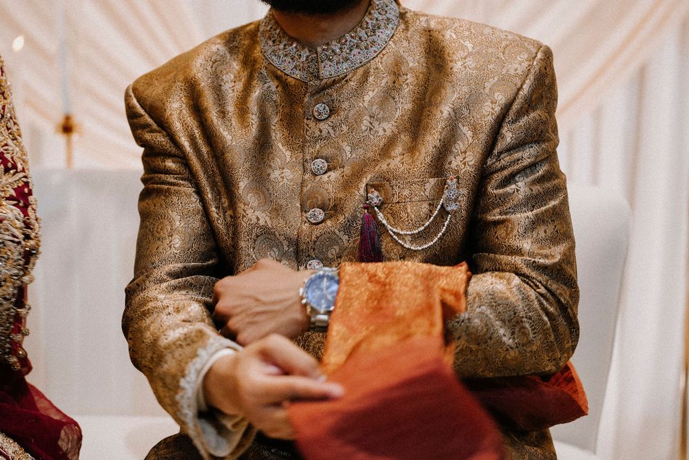 Man in ornate gold brocade sherwani holding orange envelope at Indian wedding ceremony.