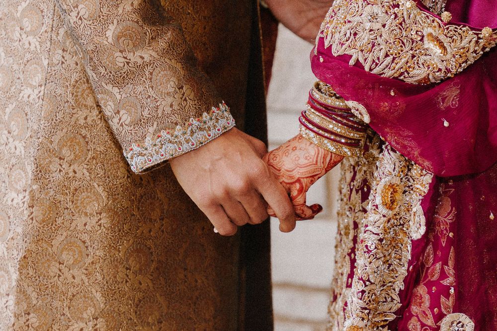 Couple in traditional South Asian wedding attire holding hands, bride with henna mehndi designs.