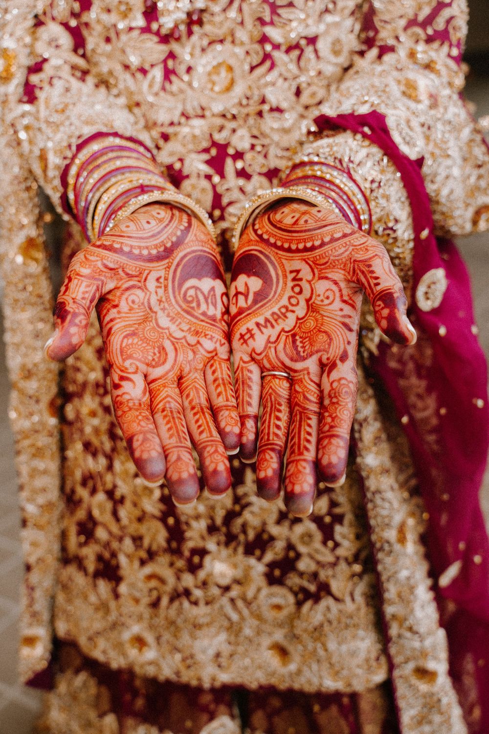 Bride displays intricate mehndi henna designs on palms with gold bangles in traditional South Asian bridal look.
