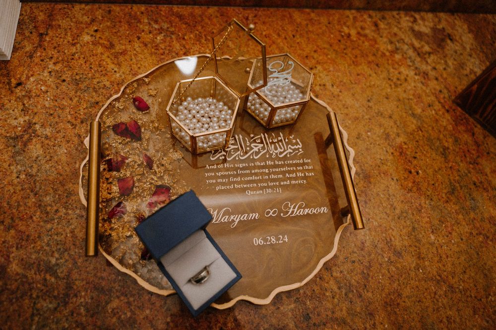 Gold mirrored tray with engraved acrylic wedding plaque, geometric candle holders, and diamond ring for Maryam and Haroon 08.26.24.