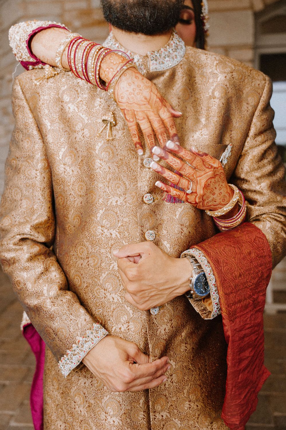 Indian bride with mehndi and bangles embracing groom in golden sherwani during traditional wedding ceremony.