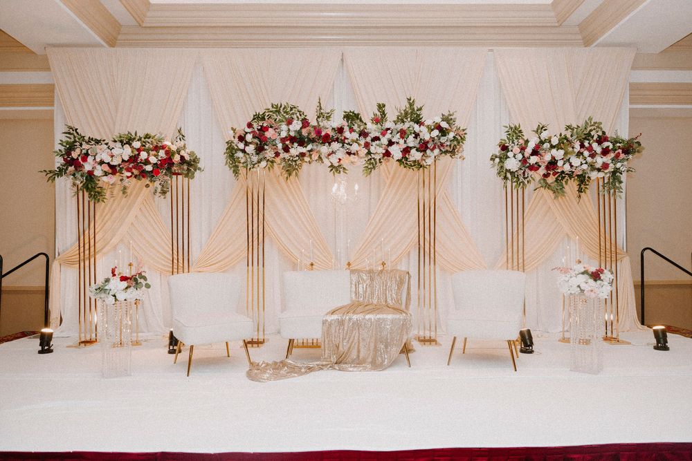 Luxurious wedding reception stage with white draping, gold accents, and lush red and white floral arrangements.