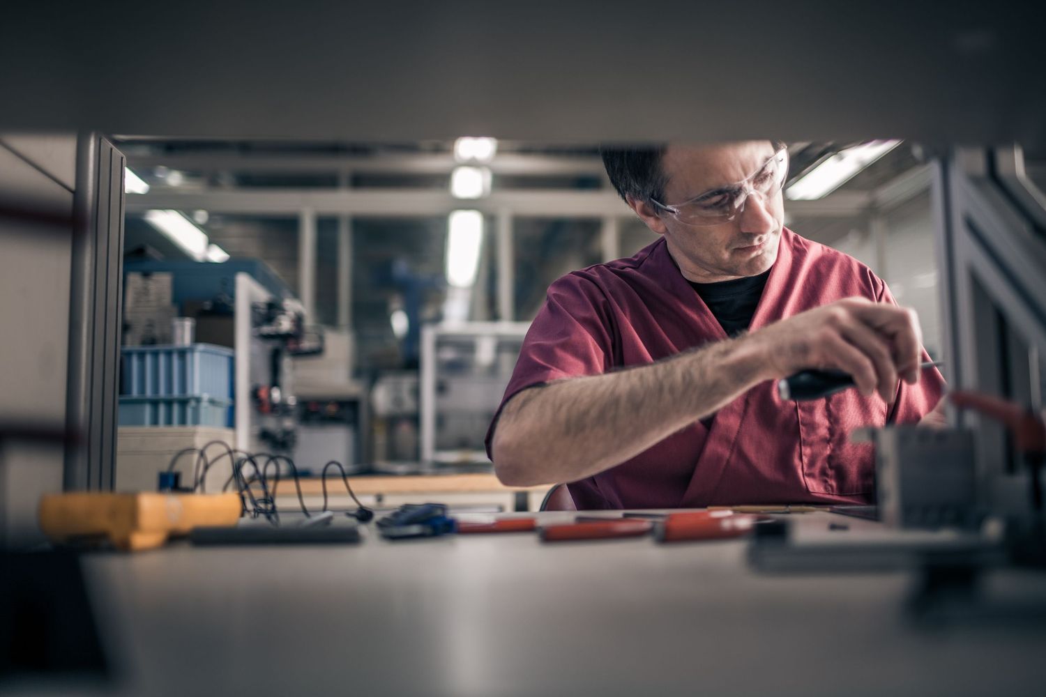 Technician in safety glasses working on electronics assembly in a professional laboratory setting.