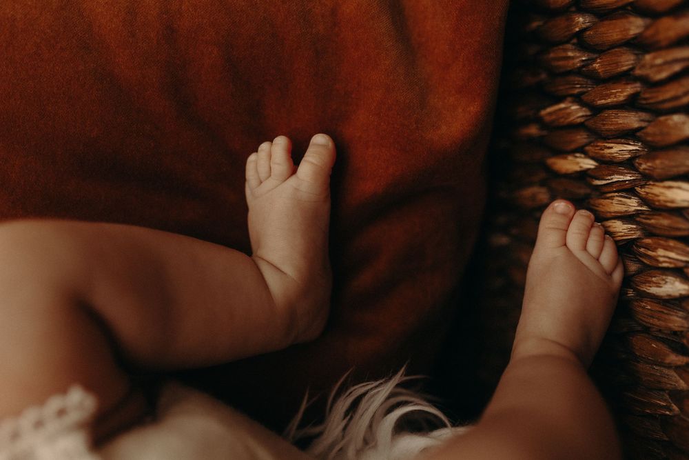Close-up of tiny newborn baby feet resting on a warm rust-colored blanket inside a woven basket.