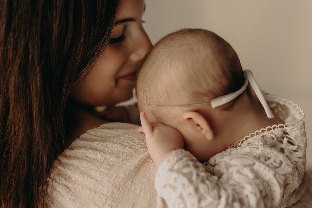 A mother tenderly holds her newborn baby, both dressed in white lace, sharing a gentle moment.