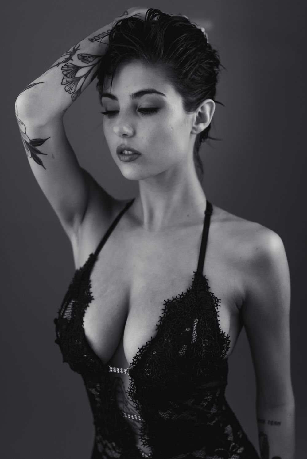 Ritratto glamour in bianco e nero della modella Giorgia Soleri in intimo di pizzo nero con scollatura profonda, mano tra i capelli e tatuagg