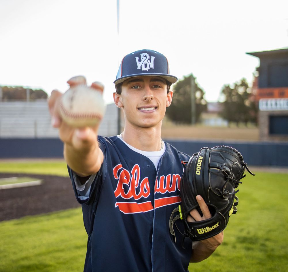 Young baseball pitcher in Blount jersey holds ball toward camera with Wilson glove on baseball field.