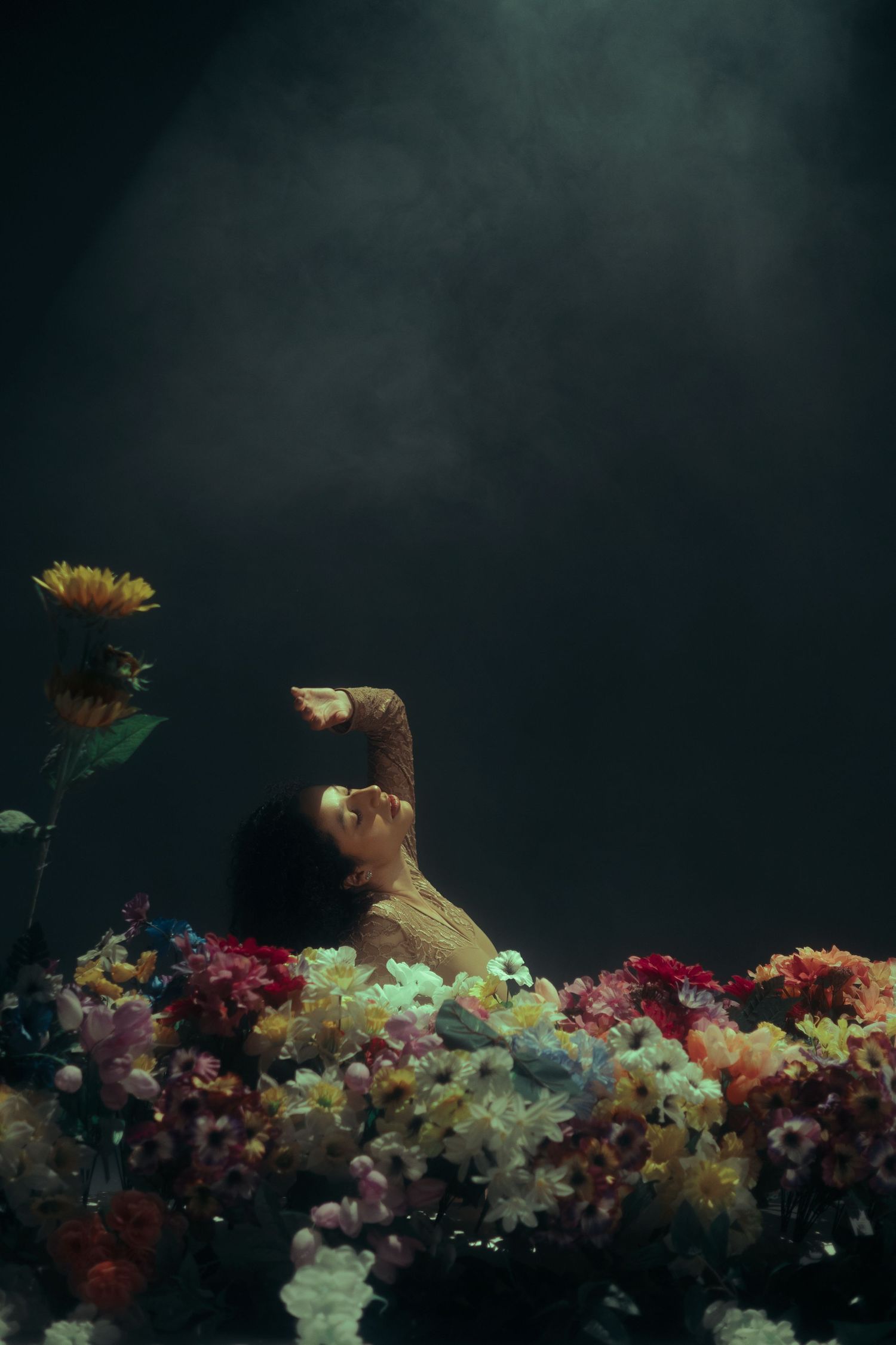 Moody fine art portrait of a woman surrounded by colorful flowers against a dark background