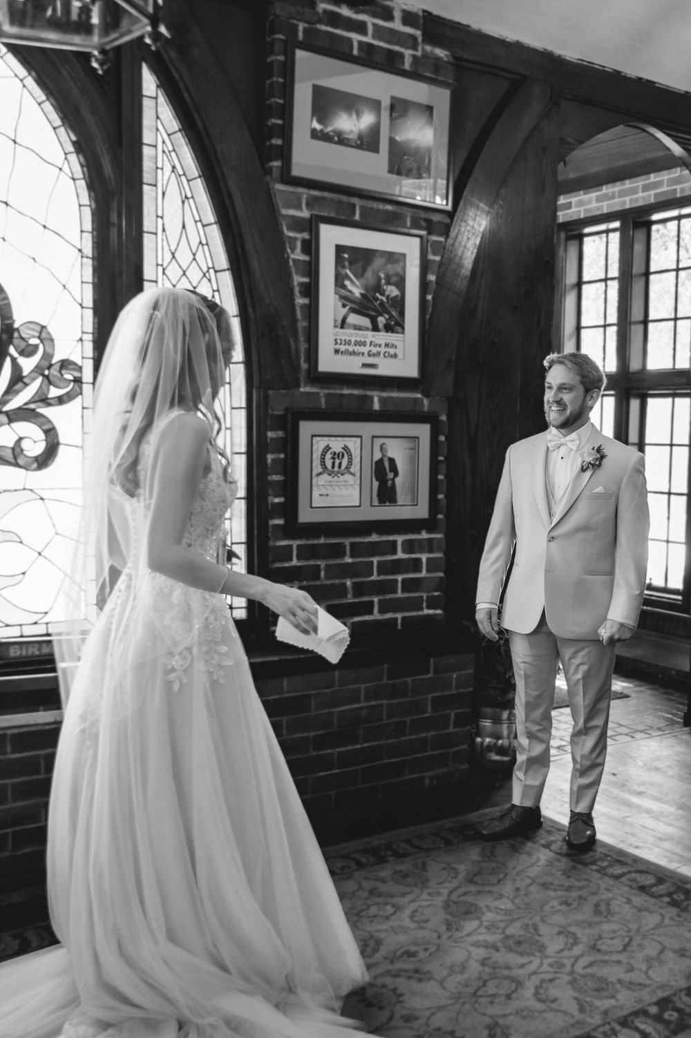 Black and white photo of a bride in a wedding gown and groom in a suit sharing a first look indoors.