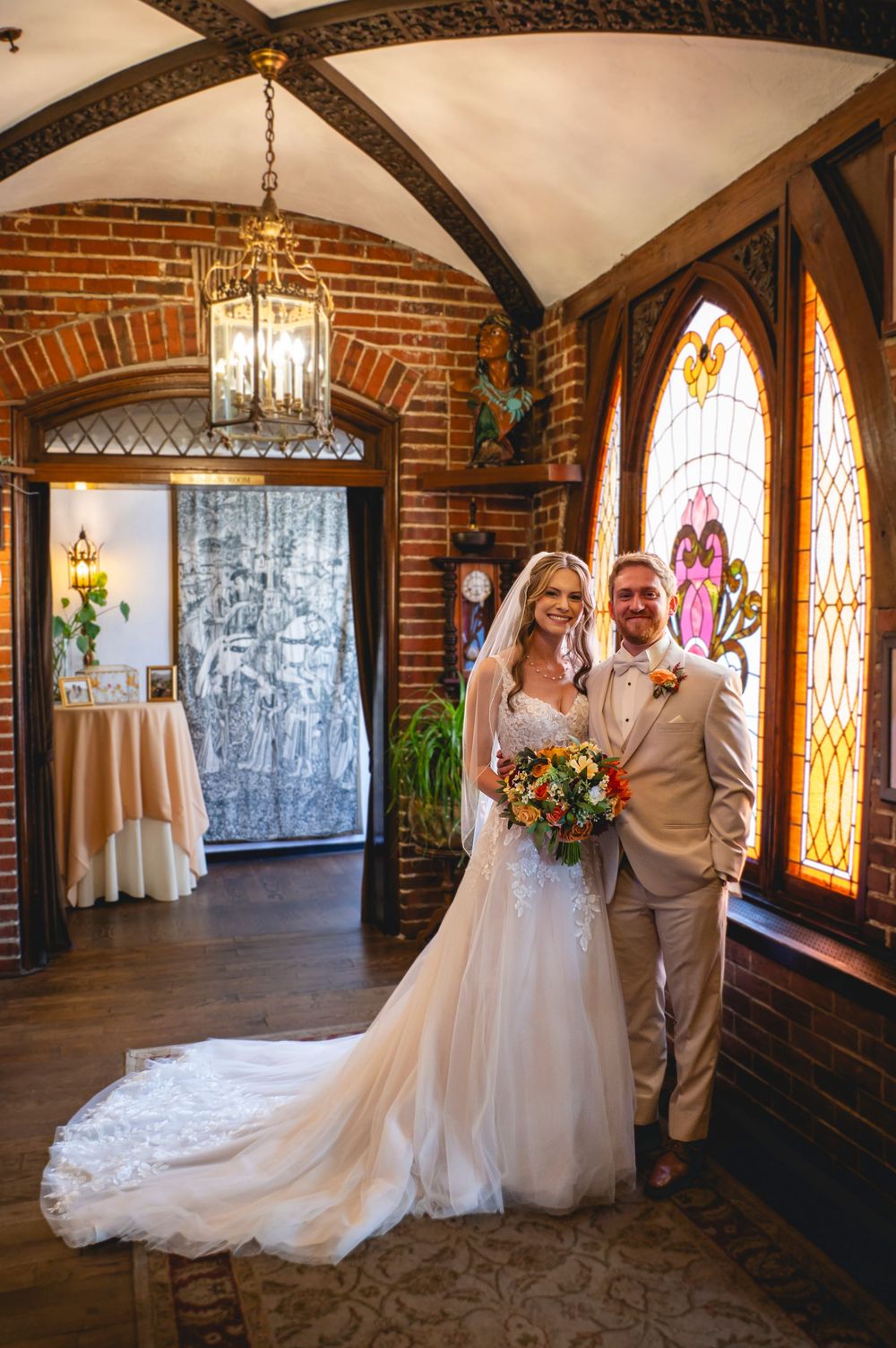 Bride and groom posing in elegant brick chapel with stained glass windows and vaulted ceiling on their wedding day.