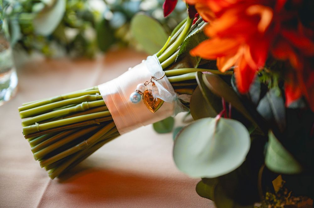 Close-up of a bridal bouquet with orange flowers, green stems tied with a decorative ribbon on a peach tablecloth.