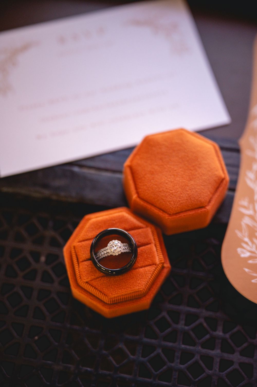 Wedding rings displayed in an orange velvet octagonal ring box beside an elegant invitation card.