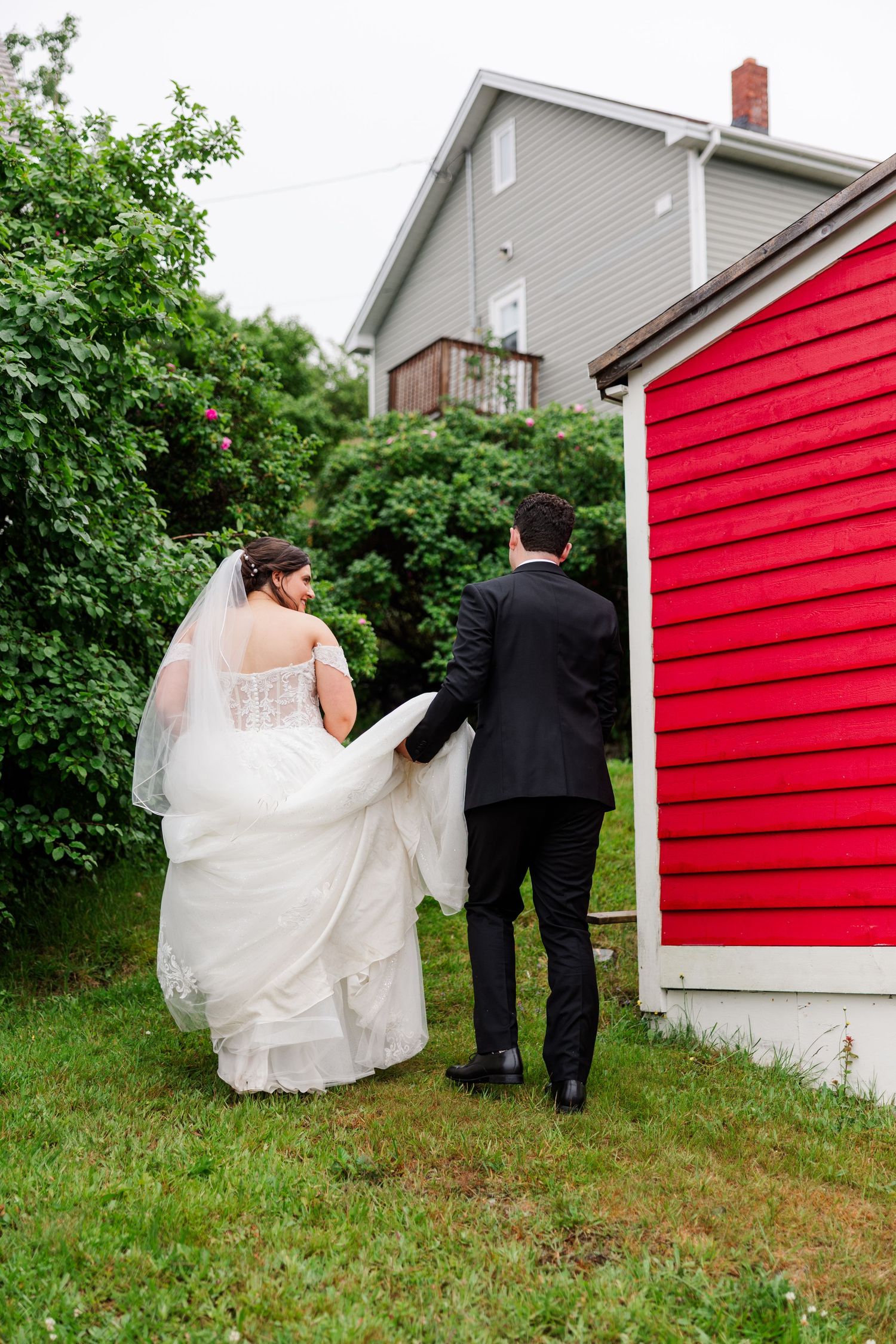 Bride and groom walking hand in hand past a red barn on their wedding day.