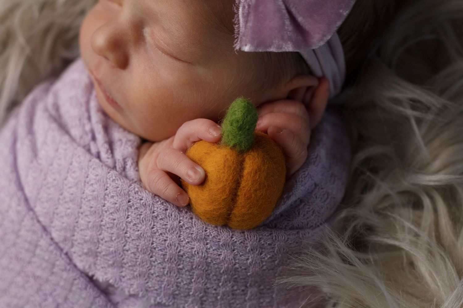 Newborn baby girl wrapped in pink knit swaddle holding teddy bear, wearing pink bow headband in wooden basket.