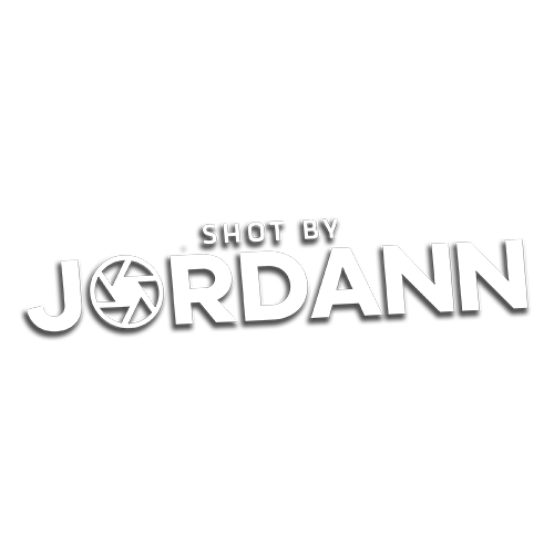 shotby.jordann photography logo with camera aperture design in white on white background.