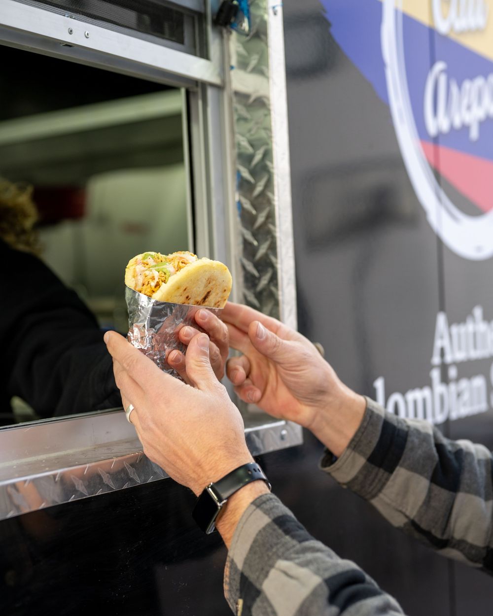Hands receiving a fresh arepa from an authentic Colombian food truck window.