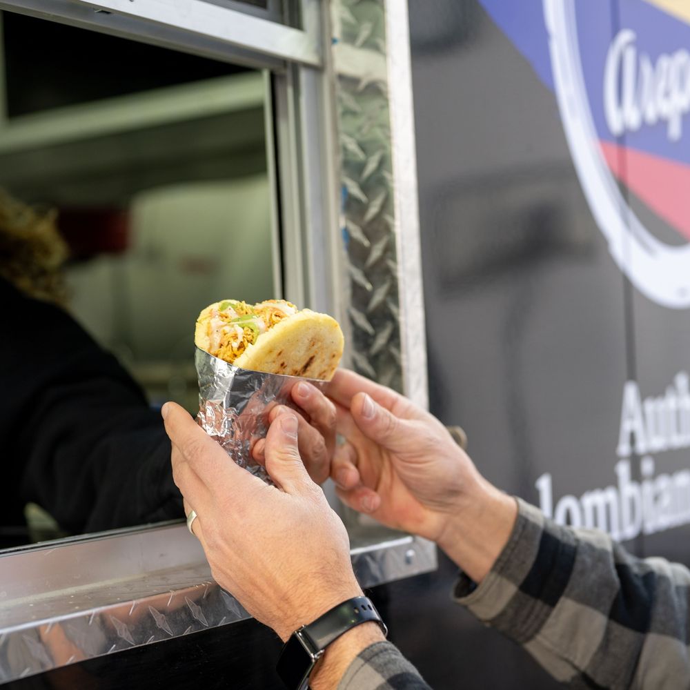 Hands receiving a fresh arepa from an authentic Colombian food truck window.