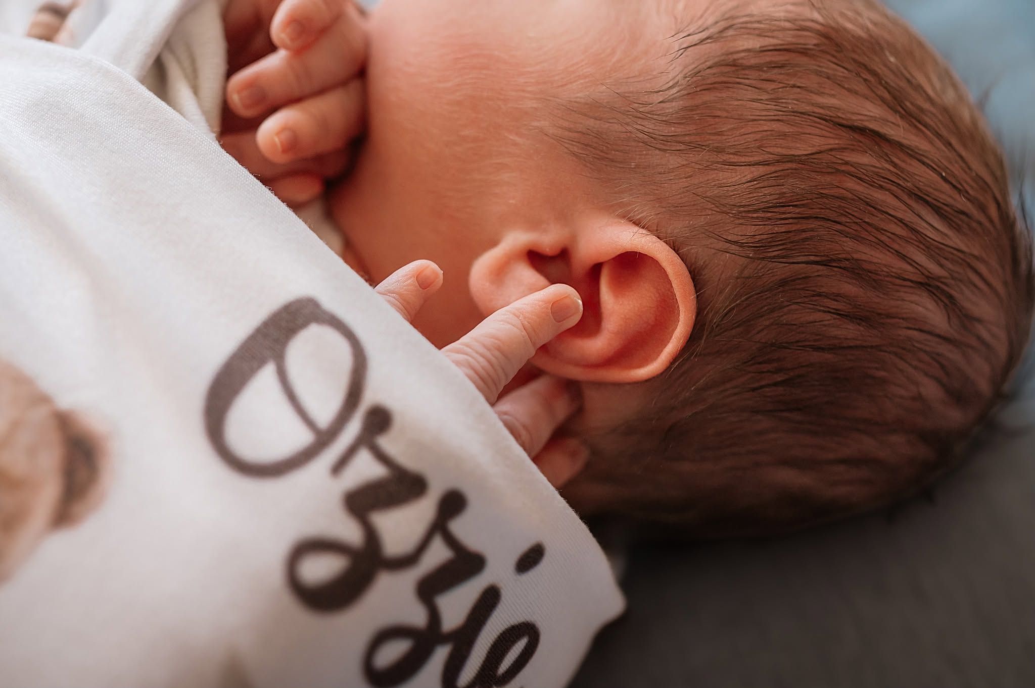 Close-up of newborn baby ear and tiny fingers clutching personalized Ozzie teddy bear swaddle blanket.