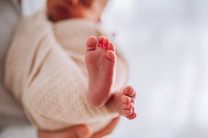 Close-up of newborn baby feet wrapped in soft cream swaddle blanket.