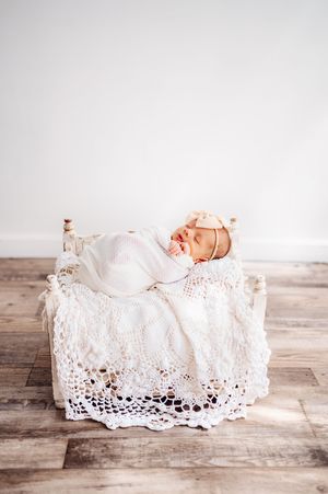 Peaceful newborn baby girl swaddled in white lace wrap sleeping in miniature vintage bed for portrait.