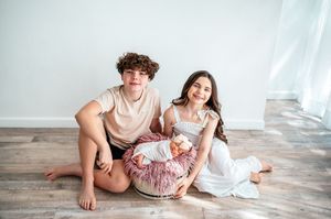 Two teenagers sit on floor smiling with newborn baby in basket.