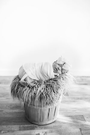 Sleeping newborn wrapped in soft knit blanket posed in rustic wooden barrel for studio portrait.
