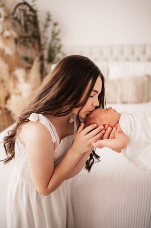Mother gently kisses her newborn baby on a white bed.