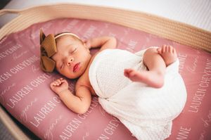 Newborn baby girl sleeping on personalized pink name blanket reading Lauren Cheyenne with bow headband.