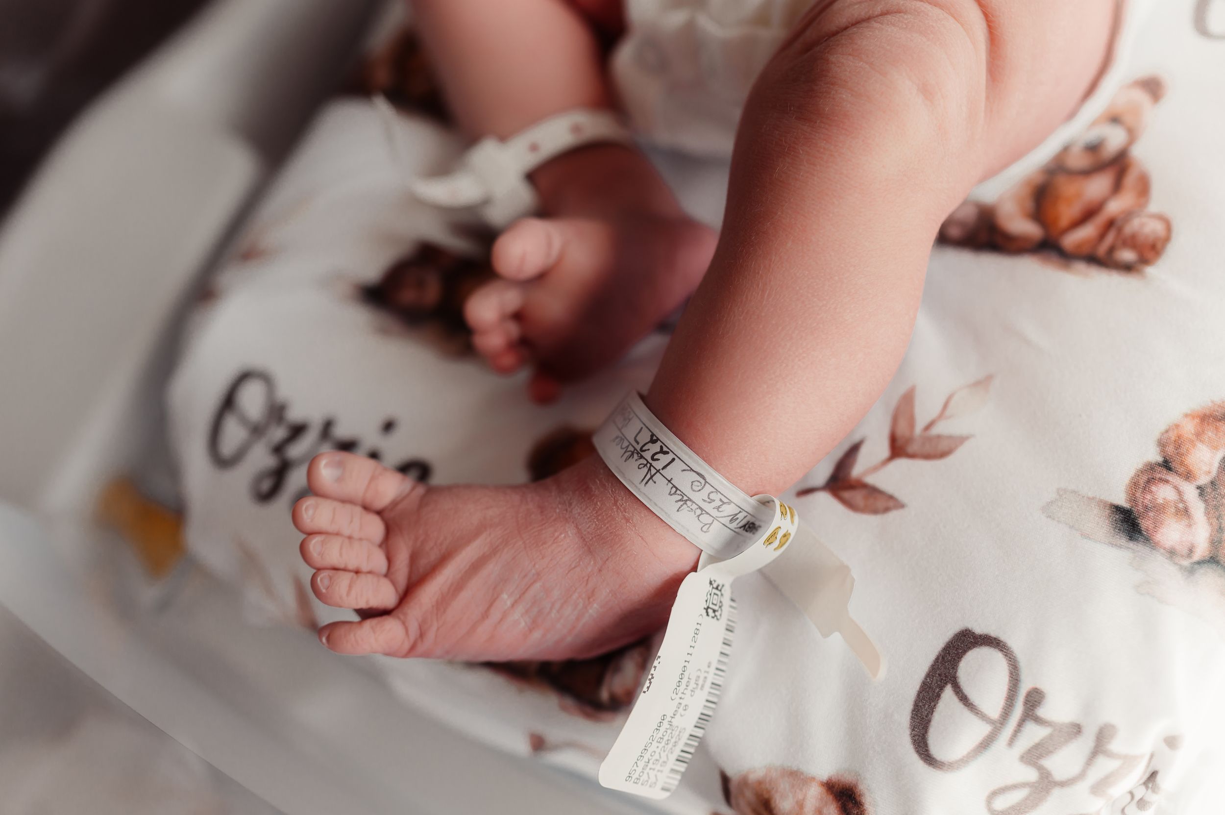 Close-up of a newborn baby's tiny feet with a hospital ID bracelet on a bear-print swaddle blanket.