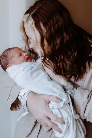 A mother with long brown hair holds her swaddled newborn baby close to her face in a tender embrace.