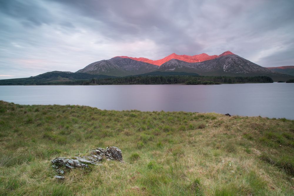 Montagne dei Twelve Bens illuminate da una luce arancione sopra il lago