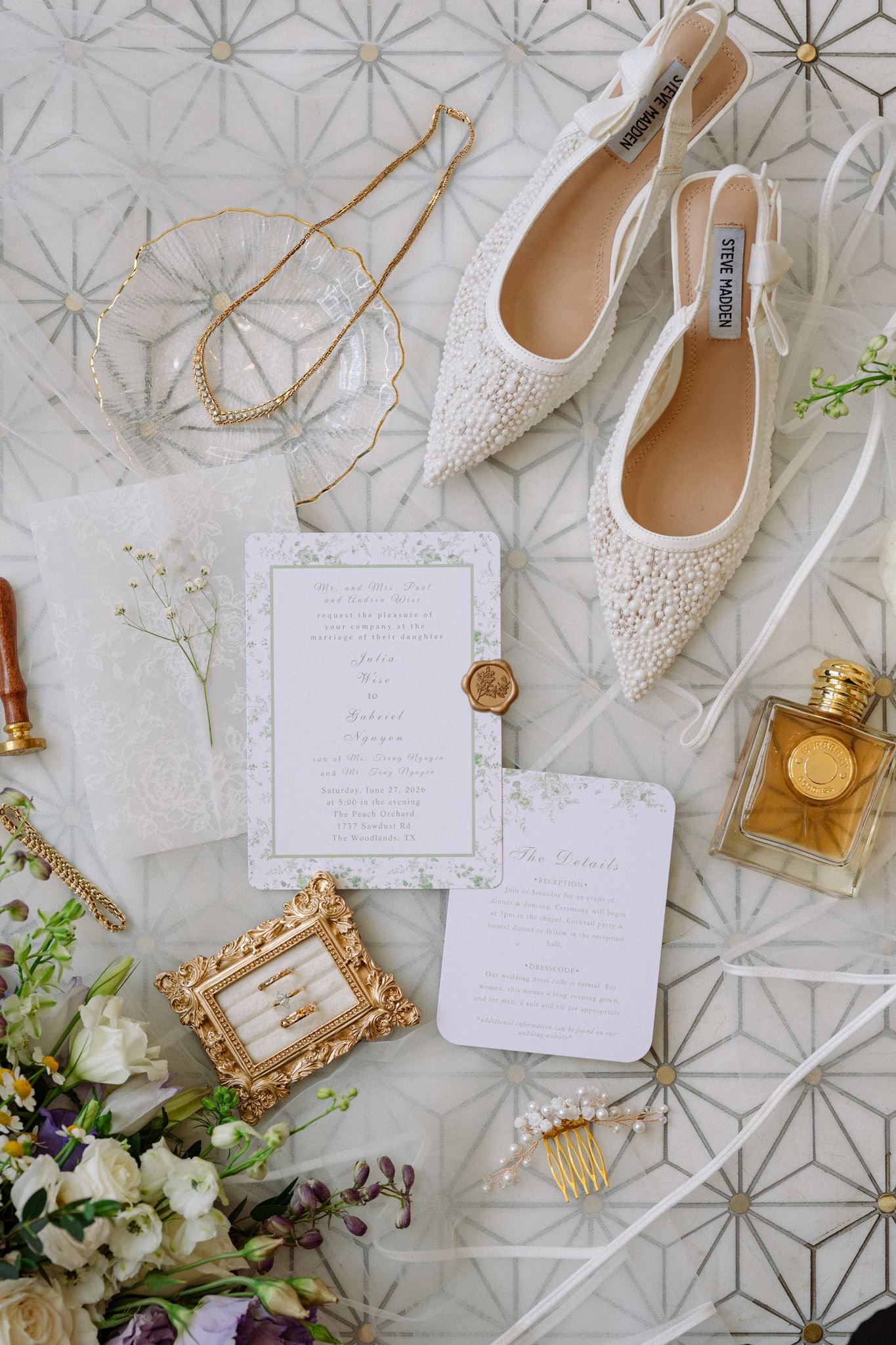 Elegant wedding flat lay featuring pearl heels, floral invitations, gold rings, perfume, and white flowers on a geometric background.