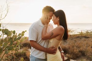Couple embracing at golden hour beach sunset, sharing a romantic moment near coastal dunes and cactus.