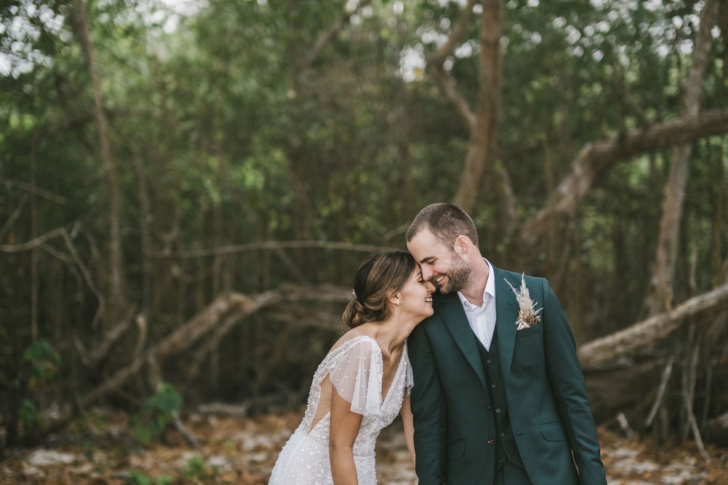 A couple in wedding attire share an intimate moment together in a wooded outdoor setting.