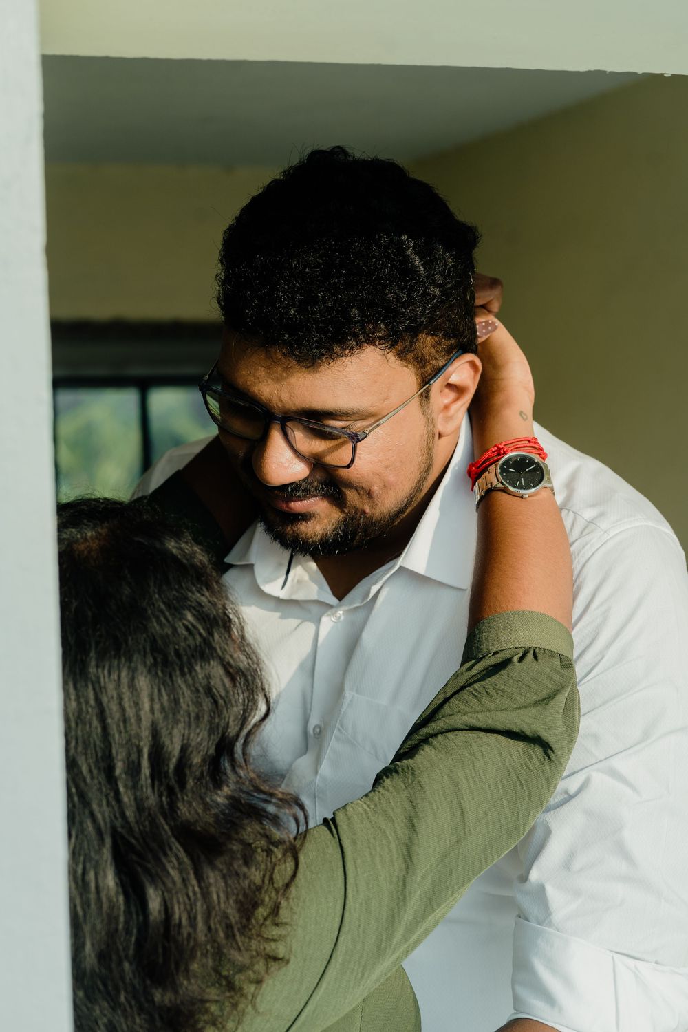 A South Asian couple shares a tender moment as a woman in green embraces a bearded man in glasses and white shirt.