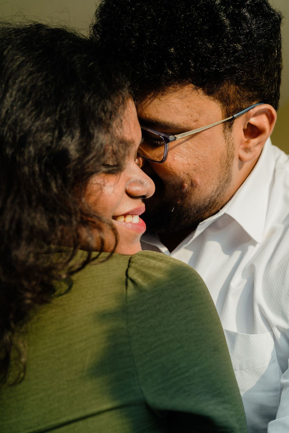 A couple sharing an intimate moment, man with glasses kissing woman's cheek as she smiles warmly.