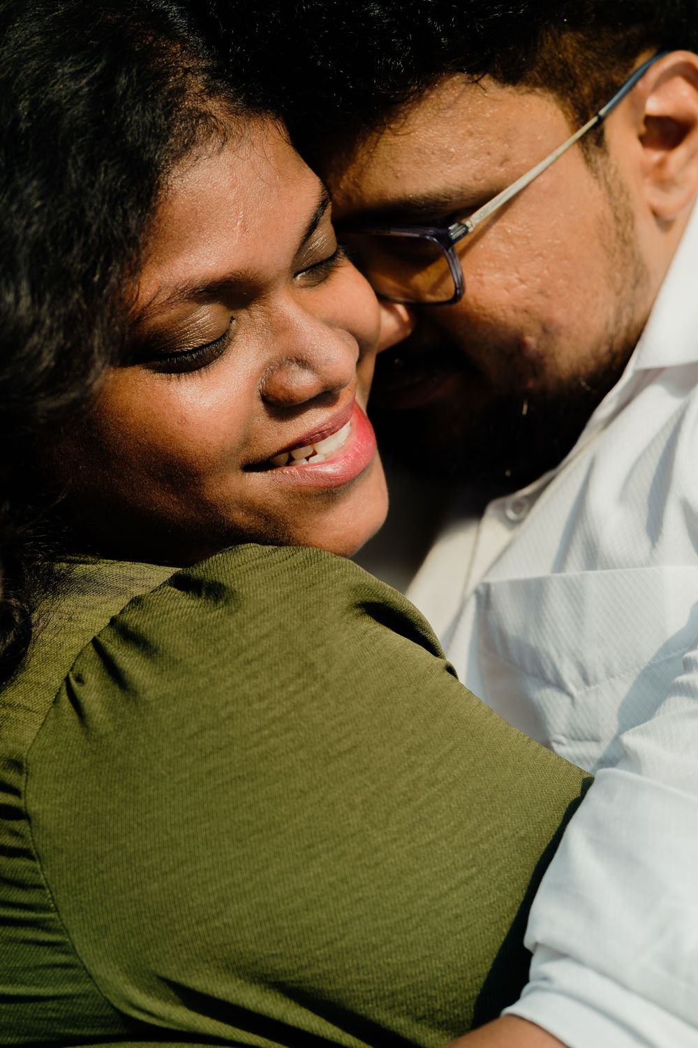 A couple sharing an intimate moment, woman in green dress smiling with eyes closed as man in glasses nuzzles her cheek.