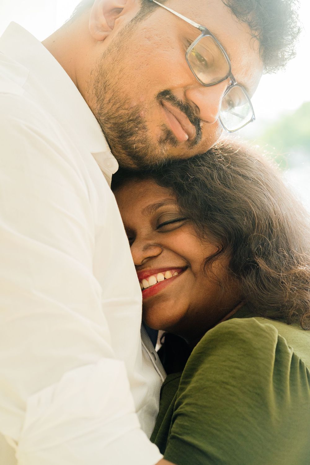 Happy Indian couple embracing, woman in green top smiling with eyes closed, man in white shirt with glasses.