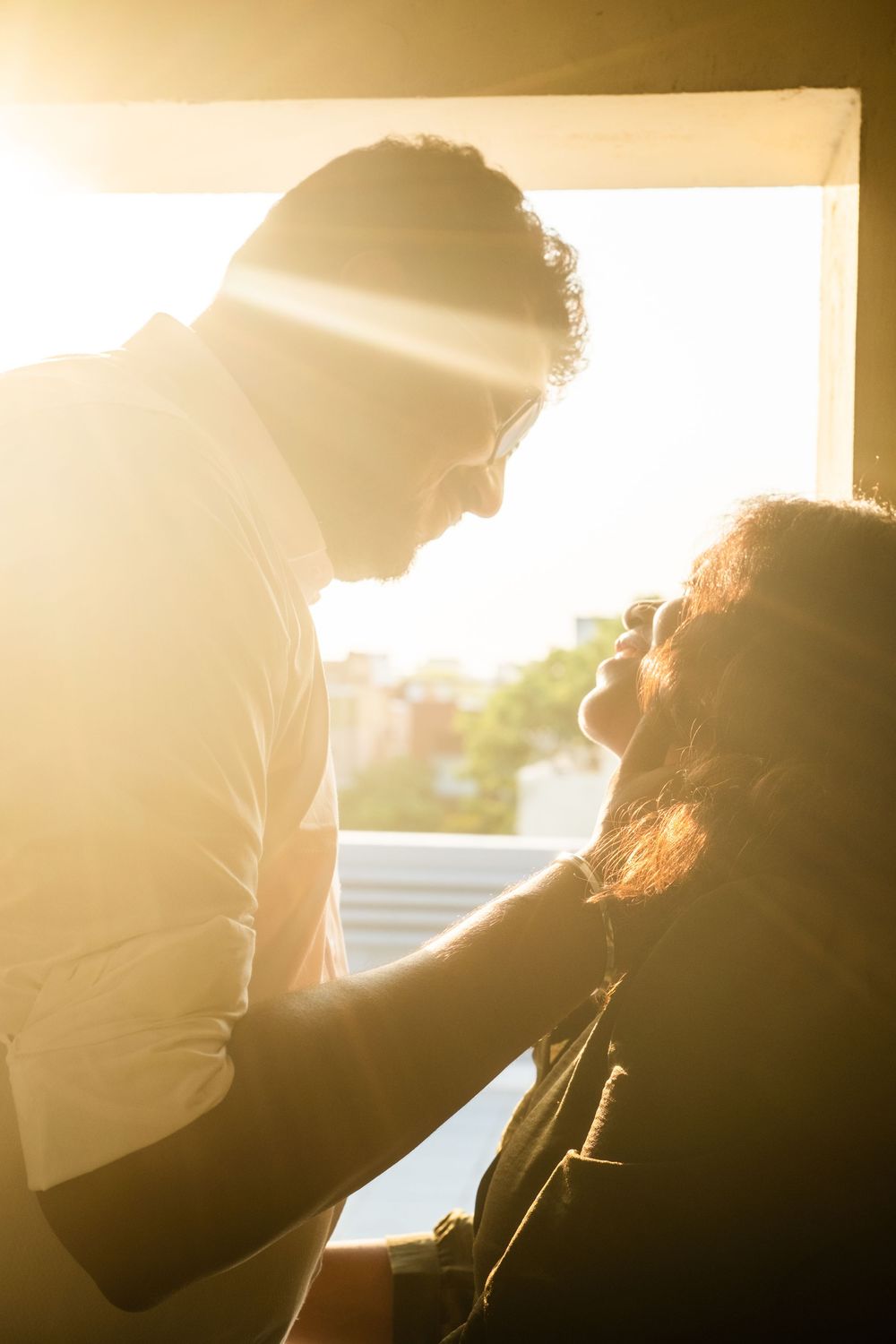Couple sharing a romantic moment backlit by golden sunlight near a window.