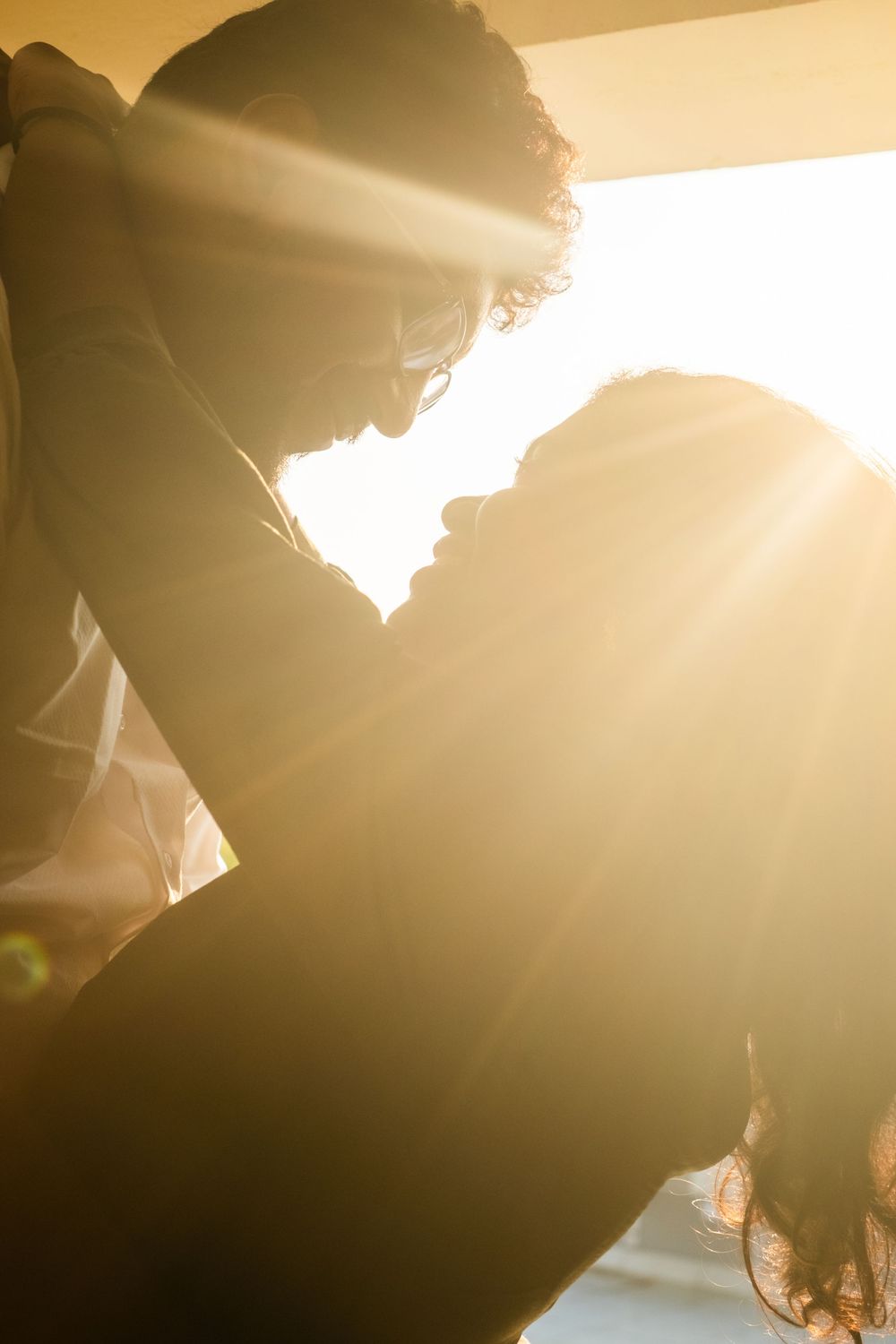 Romantic couple silhouetted against golden sunlight, leaning close together in an intimate moment.