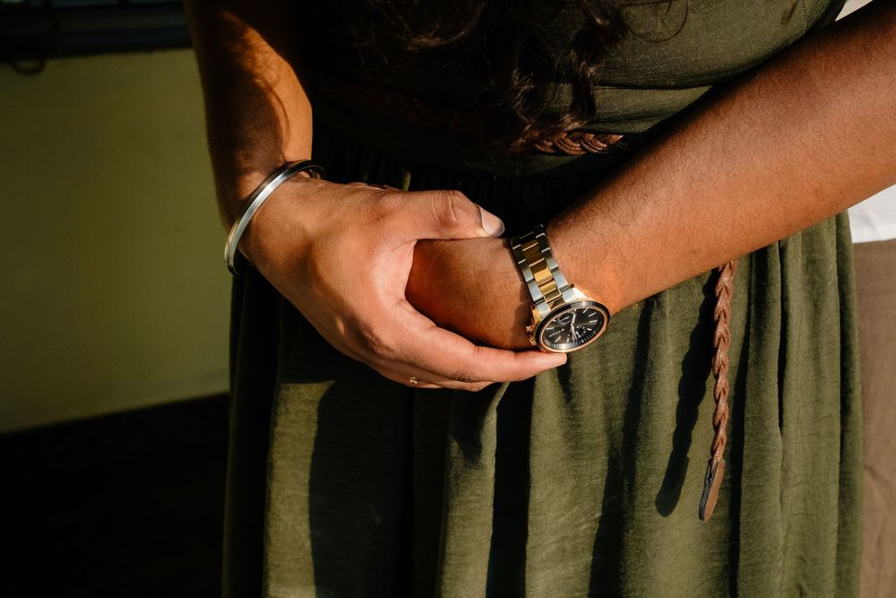 Close-up of hands clasped together wearing a silver bracelet and gold watch, paired with an olive green dress.