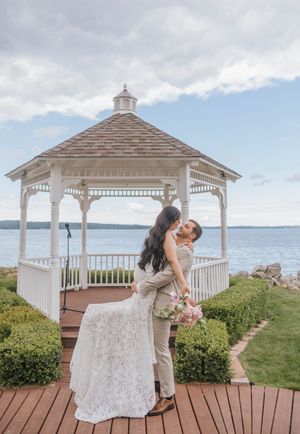 Bride and groom share a romantic kiss by a white gazebo overlooking the ocean on their wedding day.