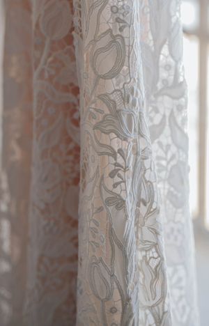 Close-up of elegant white floral lace fabric with delicate tulip and leaf embroidery patterns, softly lit by natural window light.