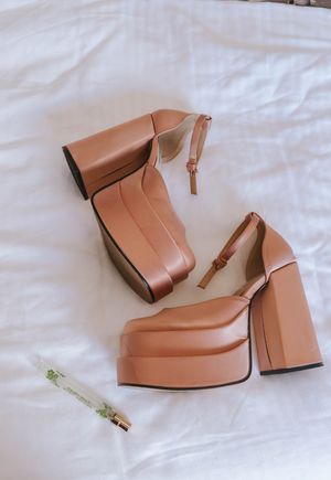 Tan leather platform heels with ankle straps and chunky block heels displayed on white fabric surface.